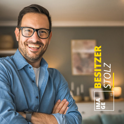 Porträt eines lächelnden Mannes mit Brille und verschränkten Armen vor einem modern gestalteten Hintergrund mit dem Text ‚Besitzer Stolz‘ im Casa Nova Design
