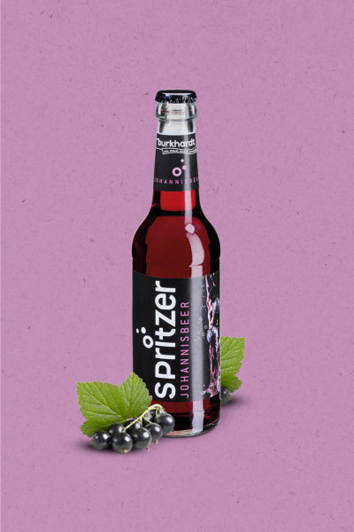 Eine 0,33l Glasflasche Burkhardt Johannisbeer Spritzer auf lila Hintergrund, davor eine Rispe frischer schwarzer Johannisbeeren mit grünen Blättern