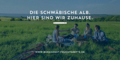 Eine Gruppe junger Freunde bei einem Picknick auf einer weiten Wiese auf der Schwäbischen Alb, ergänzt durch den Burkhardt Fruchtsäfte Slogan ‚HIER SIND WIR ZUHAUSE‘