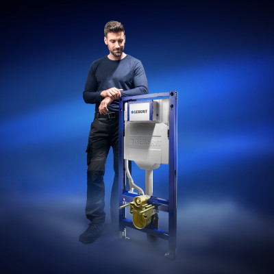 Ein lächelnder Installateur steht neben einem freistehenden Geberit Duofix vor einem blau hinterleuchteten Hintergrund