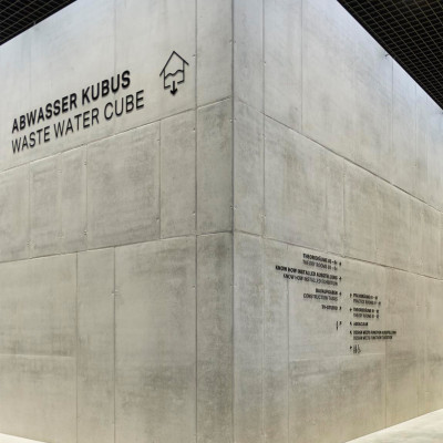 Moderne Sichtbetonwand im Geberit Campus Pfullendorf mit der großen schwarzen Signaletik ‚ABWASSER KUBUS / WASTE WATER CUBE‘ und einem detaillierten Wegeleitsystem