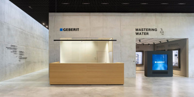 Moderner Empfangsbereich im Geberit Campus Pfullendorf mit einer hölzernen Theke vor einer Sichtbetonwand, dem Geberit-Logo und dem Schriftzug ‚MASTERING WATER‘
