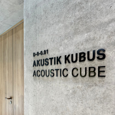 Schwarze Signaletik ‚AKUSTIK KUBUS / ACOUSTIC CUBE‘ an einer modernen Sichtbetonwand im Geberit Campus Schulungszentrum