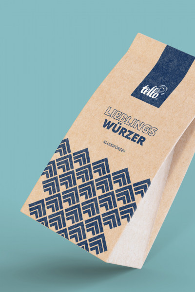 Eine braune Kraftpapier-Tüte von tellofix mit der Aufschrift ‚LIEBLINGSWÜRZER ALLESWÜRZER‘, verziert mit einem dunkelblauen grafischen Muster auf hellblauem Hintergrund