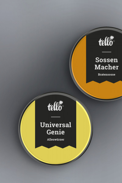 Zwei runde tellofix Gewürzdosen in der Draufsicht auf grauem Grund: Eine gelbe Dose ‚Universal Genie Alleswürzer‘ und eine orangefarbene Dose ‚Sossen Macher Bratensosse‘, beide mit schwarzem Banner-Etikett